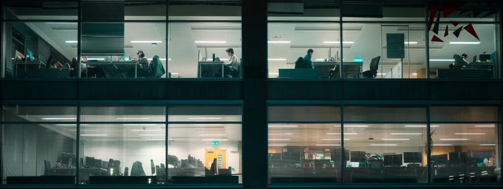 Office windows at night, showing workers and empty desks
